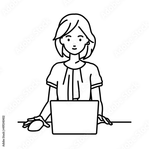 デスクで座ってPCを使っているオフィスカジュアルの女性
