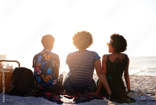 Friends are the ones that make life worth living. Rearview shot of an unrecognizable diverse trio of women having a picnic on the beach during the day.