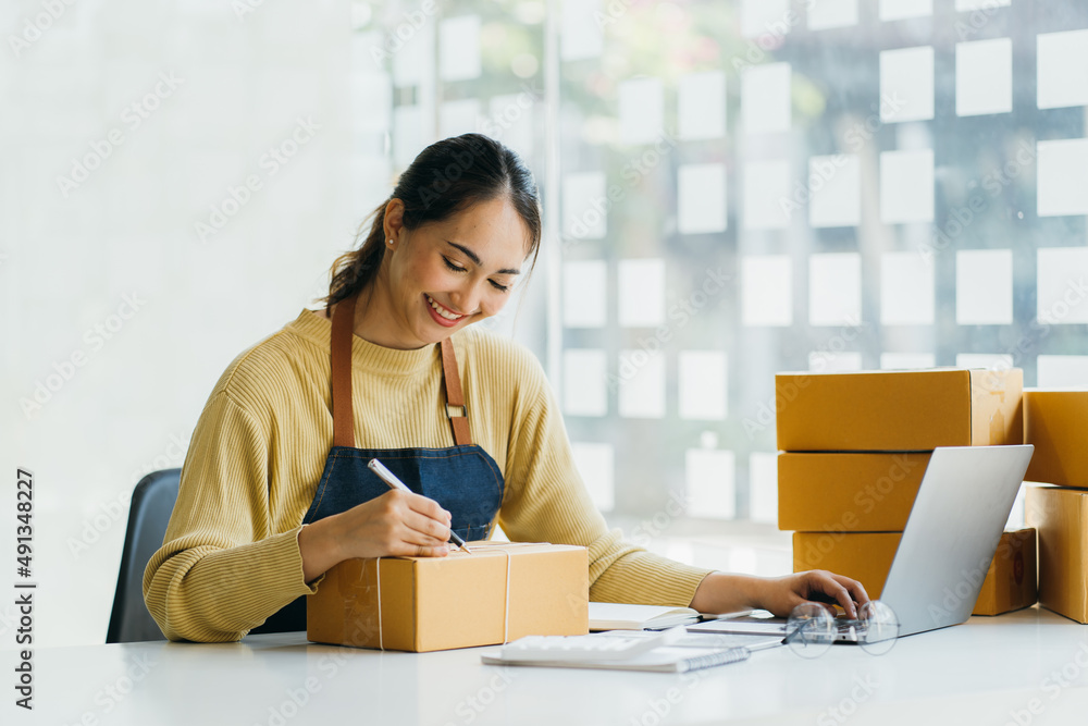Starting Small business entrepreneur SME freelance,Portrait young woman working at home office, BOX,smartphone,laptop, online, marketing, packaging, delivery, SME, e-commerce concept