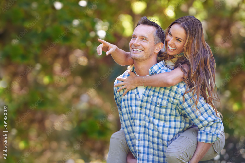 Look over there. A handsome man giving his wife a piggyback outdoors. Look over there. A handsome man giving his wife a piggyback outdoors.