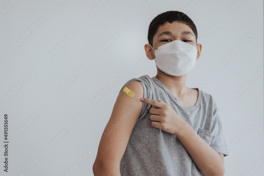 Asian boy showing shoulders after getting a vaccine. Happy little boy showing arm with band-aids on after vaccine injection.