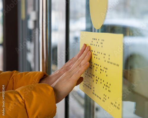 Close-up of a woman reading a braille lettering on a glass door.