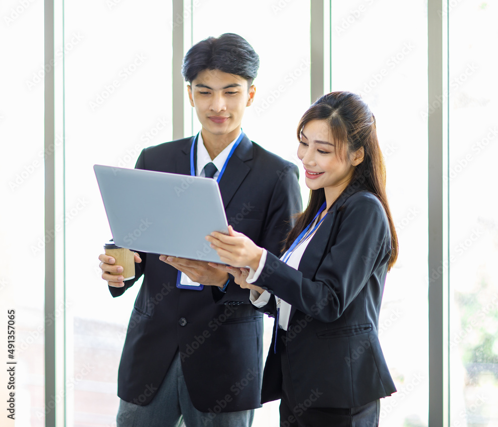 Asian young male professional successful businessman manager looking at laptop computer explaining to female secretary employee staff in formal suit in company office workplace.