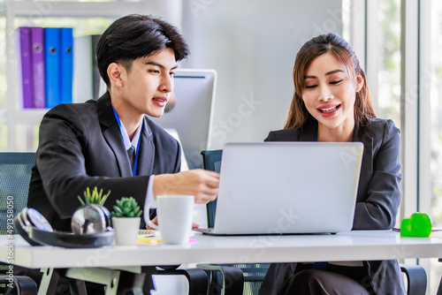 Asian young happy professional male businessman mentor and female businesswoman colleague in formal suit working discussing meeting together at workplace desk with laptop notebook computer in office