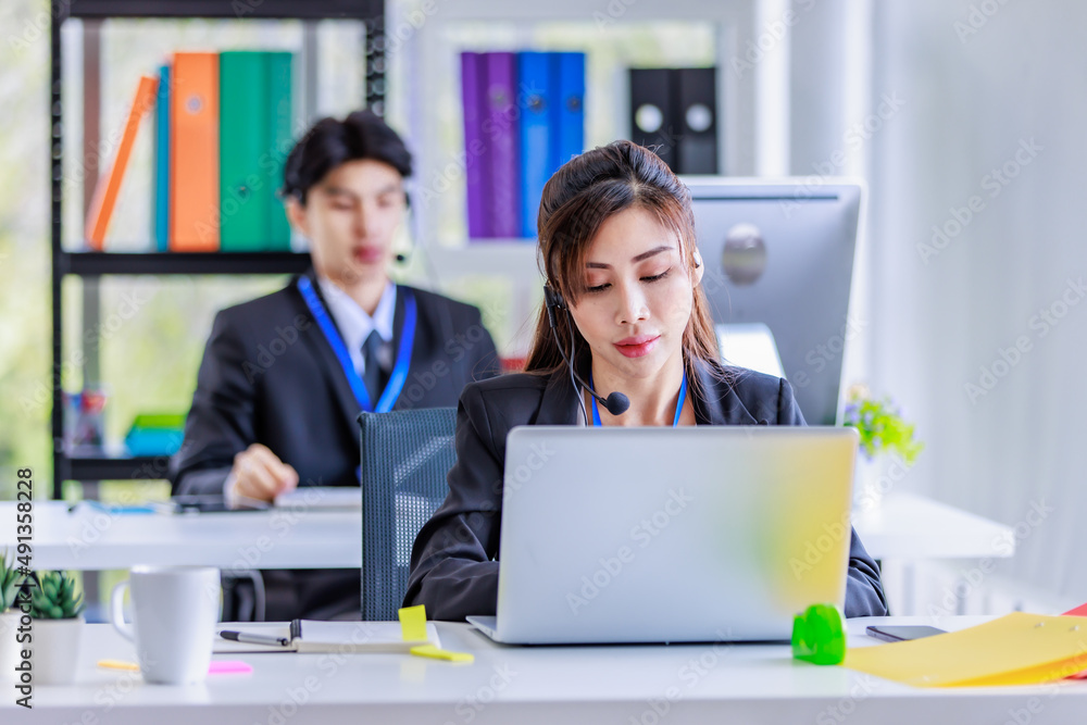 Asian young beautiful female businesswoman operator wearing headset with microphone working at helpdesk service with male colleague via laptop computer helping consulting with customers call center Asian young beautiful female businesswoman operator wearing headset with microphone working at helpdesk service with male colleague via laptop computer helping consulting with customers call center