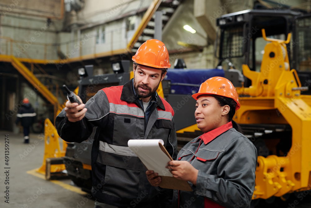 Two interracial workers of industrial plant discussing new equipment for machinery production while foreman pointing forwards Two interracial workers of industrial plant discussing new equipment for machinery production while foreman pointing forwards