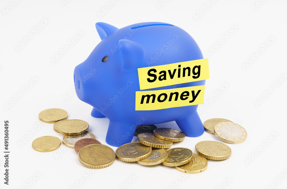 Φωτογραφία On the table are coins and a blue piggy bank with the inscription - SAVING MONEY