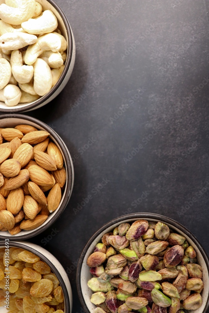 Various varieties of nuts and dried fruits are in a bowls on black background. Top view. Healthy food. Vegetarian nutrition. cashew, almond, pistachio, and raisins. Assorted nuts banner. Copy space Various varieties of nuts and dried fruits are in a bowls on black background. Top view. Healthy food. Vegetarian nutrition. cashew, almond, pistachio, and raisins. Assorted nuts banner. Copy space