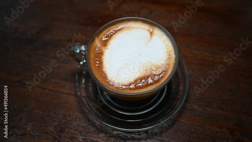 Cappuccino served with a glass cup and saucer on a wooden table at a Thai restaurant. photo