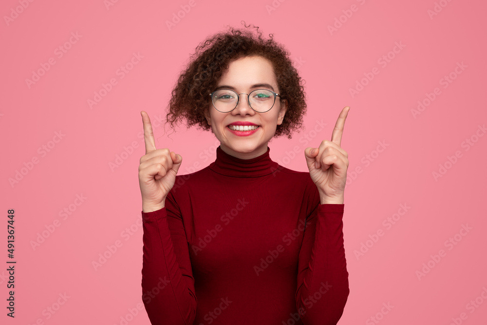 Cheerful young woman pointing up and smiling at camera Cheerful young woman pointing up and smiling at camera