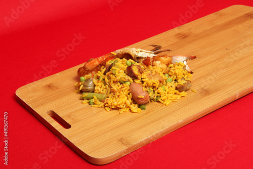 Dish from Valencia Spain Arroz a la paella on a wooden board in a red background ready to eat prepared with saffron, seafood, shrimp, vegetables
