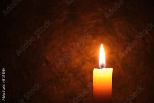 Burning candle against a dark concrete wall.