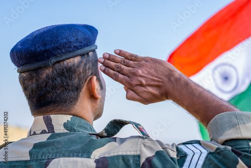 back view shot of Proud Indian army soldier saluting by looking indian flag - concept of patriotic, nationalism and honour