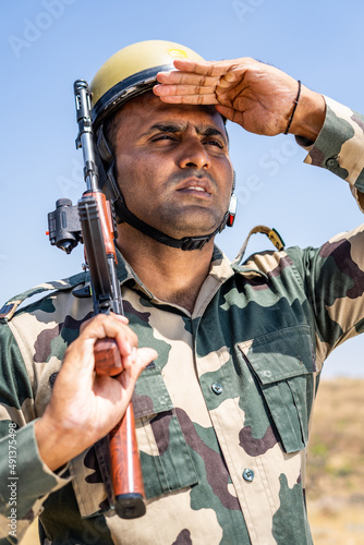 Fotografiet Soldier with gun hand looking around on hill top with flying indian flag in back