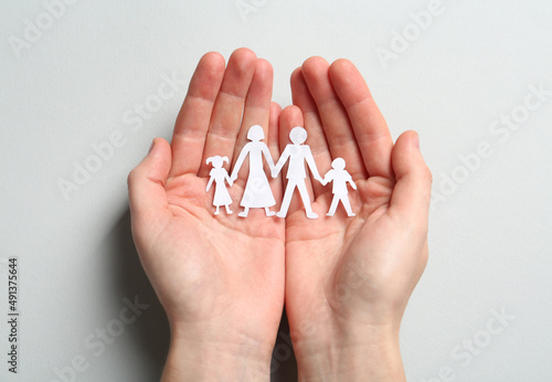 Woman holding paper cutout of family on light background, top view