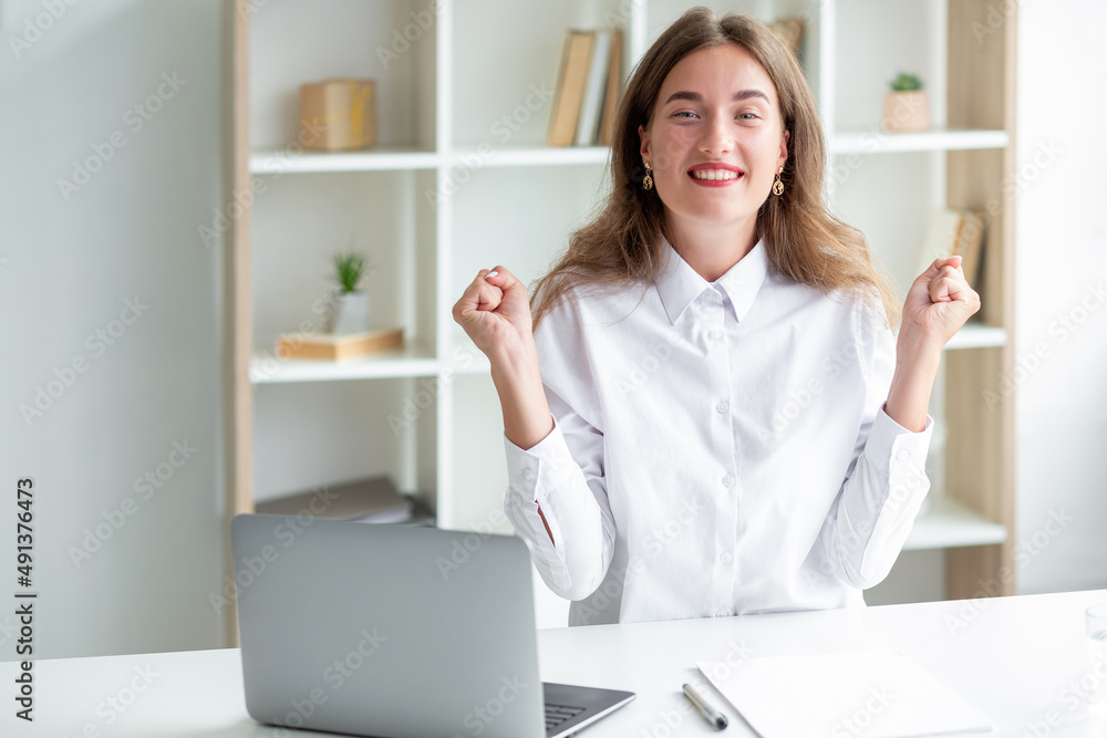 Expressive joy. Office happy woman. Work inspiration. Excited lady in white shirt sitting desk with laptop hands up light room interior. Expressive joy. Office happy woman. Work inspiration. Excited lady in white shirt sitting desk with laptop hands up light room interior.