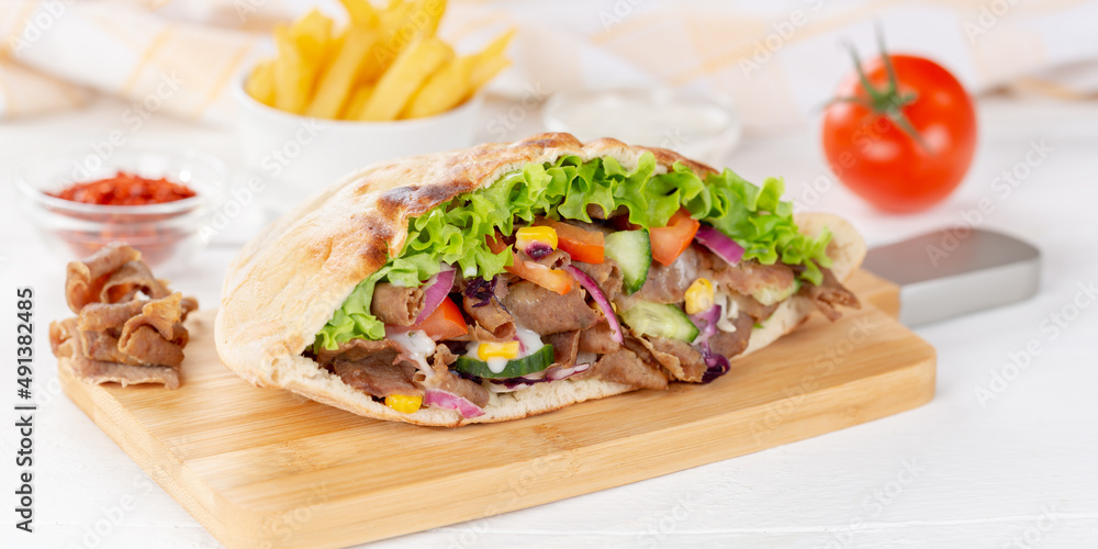 Döner Kebab Doner Kebap slice fast food in flatbread with French Fries on a wooden board panorama Döner Kebab Doner Kebap slice fast food in flatbread with French Fries on a wooden board panorama
