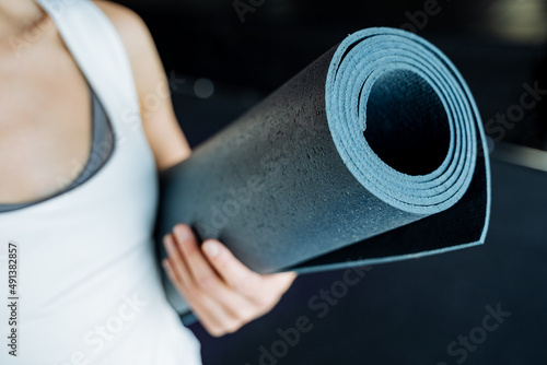 The sight of a girl holding a yoga mat in her hands. Rolled up blue mat. Sports equipment for fitness.