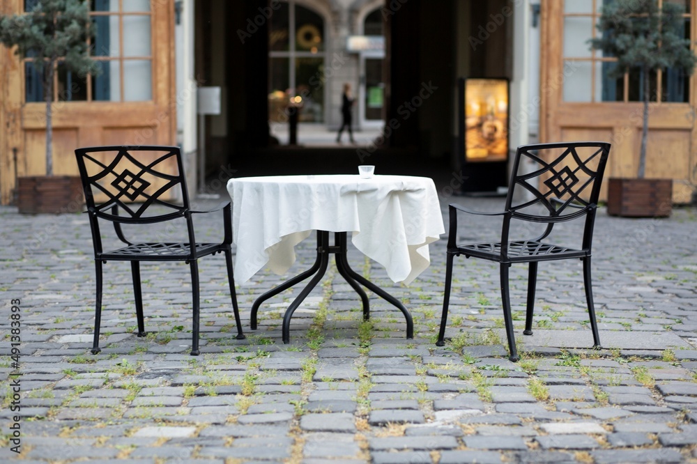 Two chairs and a table covered in white cloth in a cobble-stoned yard.