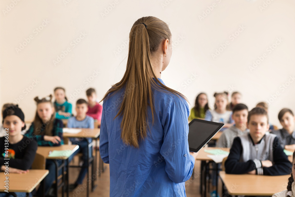 Teacher asking her students a question at the elementary school with tablet computer