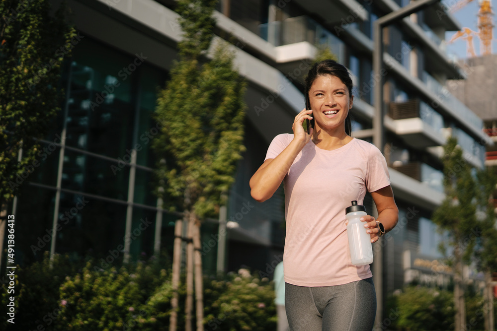 Fit athlete woman in sportswear outdoors. Young woman talking to the phone.