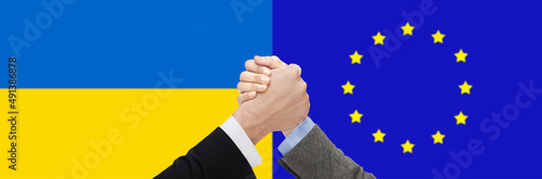 political, business and national concept - close up of arm wrestling over flag of ukraine and european union on background
