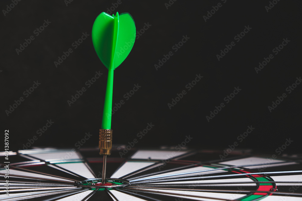 Dartboard with green dart stuck in center. Dartboard with green dart stuck in center.