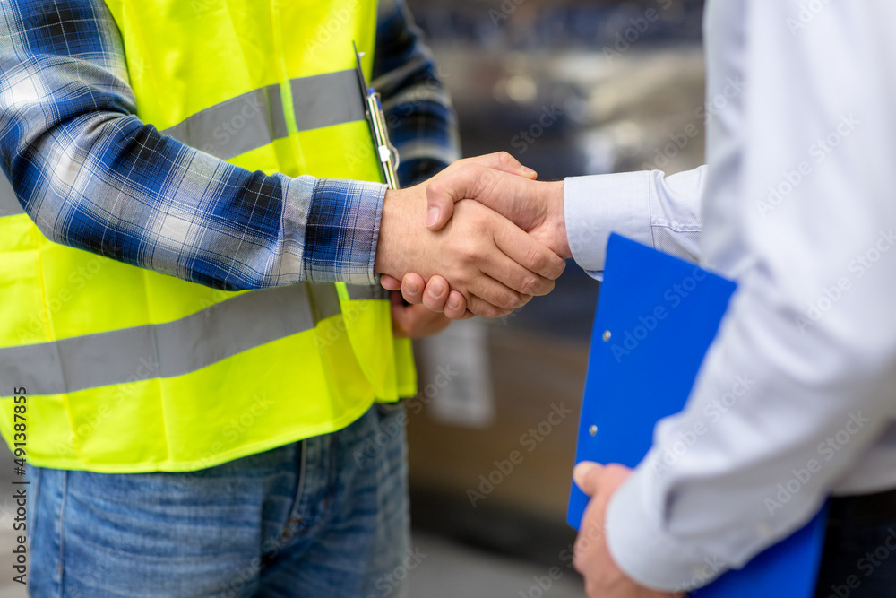 logistic business and cooperation concept - close up of manual worker and businessman with clipboard shaking hands and making deal at warehouse
