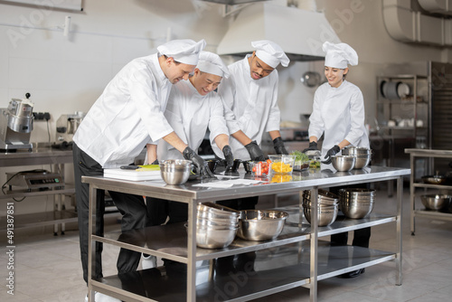 Multiracial team of cooks mixing ingredients for take away food in professional kitchen. Concept of dark kitchen for cooking for delivery. Idea of teamwork in a restaurant. Diverse people at job