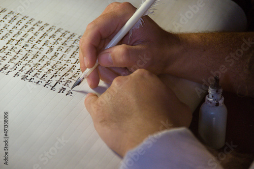 Closeup view of the hands of a Jewish scribe writing the Hebrew text of the Torah or Bible on parchment using a feather quill and black ink. photo