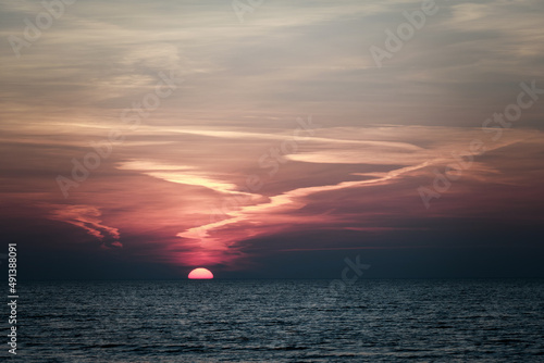 sun setting in the sea with cloud trails