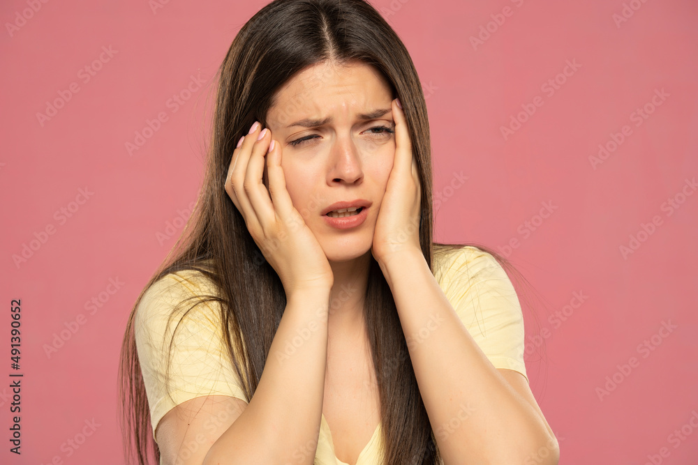 Portrait of beautiful young brunette with yellow shirt touching her temples feeling stress, on pink background Portrait of beautiful young brunette with yellow shirt touching her temples feeling stress, on pink background
