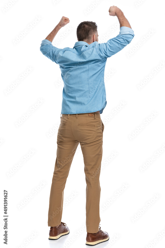 excited young man in denim shirt holding fists above head excited young man in denim shirt holding fists above head