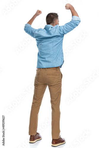 excited young man in denim shirt holding fists above head