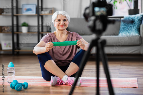 fitness, sport and video blogging concept - happy senior woman or blogger with camera and resistance loop streaming online class at home