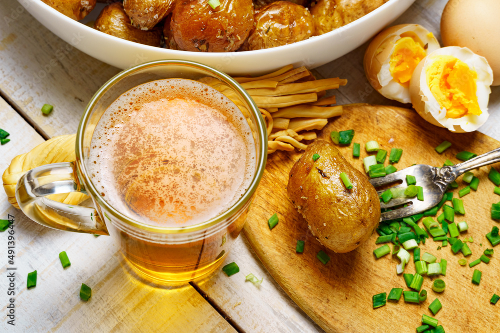 tasty food in rural style, - glass of beer, fried chicken meat and potatoes, garlic and green onions, cheese, boiled eggs and salt, cooked food on a white wooden boards tasty food in rural style, - glass of beer, fried chicken meat and potatoes, garlic and green onions, cheese, boiled eggs and salt, cooked food on a white wooden boards