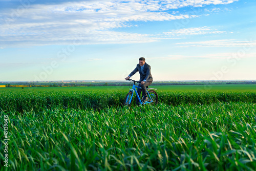 businessman rides a bicycle through a green grass field, dressed in a business suit, beautiful nature in spring, business concept