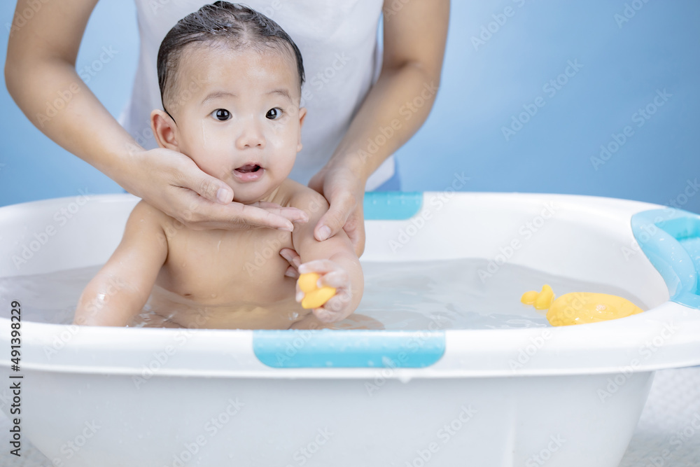cute cheerful baby and mother play in bath with toy on blue background cute cheerful baby and mother play in bath with toy on blue background