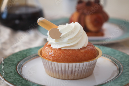 Close up of French baba au rhum topped with mousse white vanilla cream and a tube of rhum on it. It's a yeast dough sponge cake, baked in a ring mold, and soaked in rum. With coffee in background photo