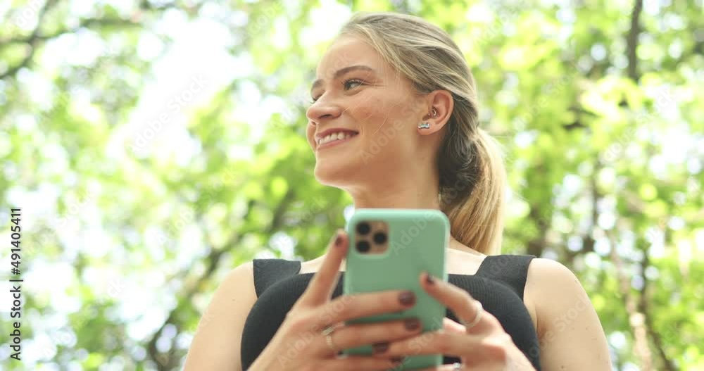 Young woman using a smartphone at day time with a green park. High quality video. Mobile phone, technology, urban concept. Young woman using a smartphone at day time with a green park. High quality video. Mobile phone, technology, urban concept.