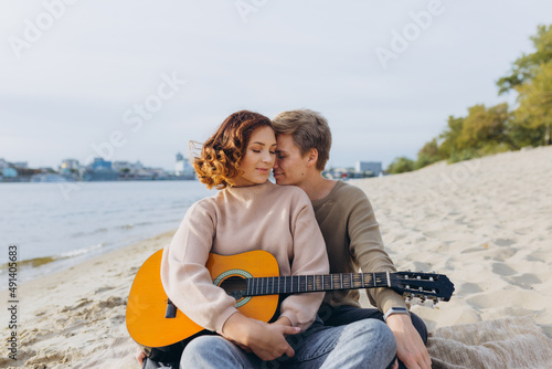 young guy teaching his girlfriend how to play guitar, self-taught. Couple in love having fun on the beach hugging and kissing
