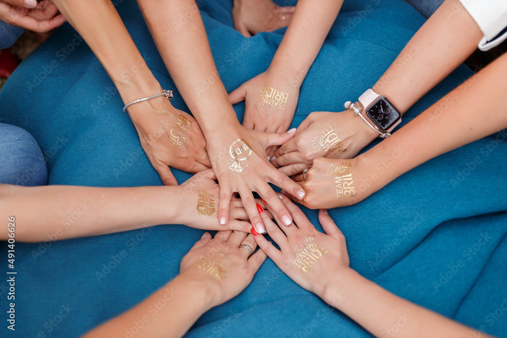 Fototapeta premium Hands of young girls with manicure without faces folded in the center with the inscriptions team of the bride in gold letters. bachelorette party celebration