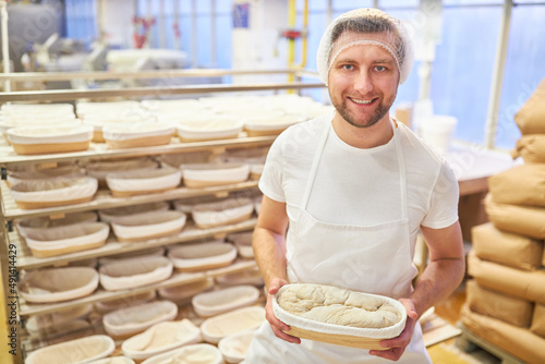 Lächelnder junger Mann als Bäcker zeigt einen Laib Brot