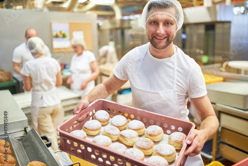 Bäcker Lehrling trägt frische Pfannkuchen in der Bäckerei