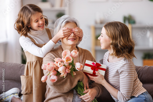 Happy International Mother's Day.Smiling  daughter and granddaughter giving flowers  and gift to grandmother   celebrate spring holiday Women's Day at home photo