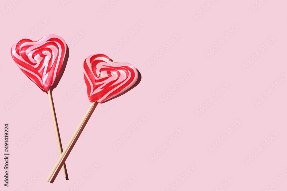 two heart-shaped lollipops on a pink background, copy space for text, Red and whie striped sweet lollipops.
