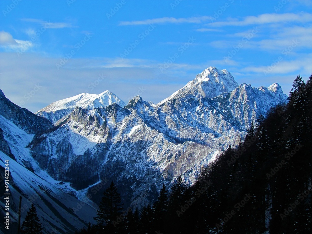 Scenic view of mountain Vrtaca with mountain Stol in Karavanke mountains in Gorenjska region of Slovenia the back lit by the sun in winter with snow covering the slopes taken from Planina Korosica