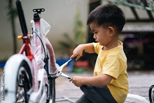 Cute asian little toddler boy is trying help father to assemble new bicycle by himself, concept of learning, practice and practical life skill for kid education and development at home in family life.