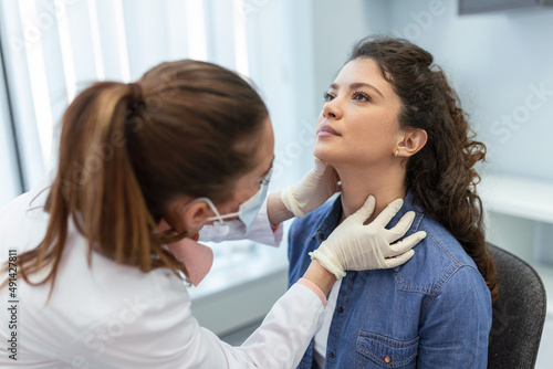 medicine, healthcare and medical exam concept - doctor or nurse checking patient's tonsils at hospital. Endocrinologist examining throat of young woman in clinic photo