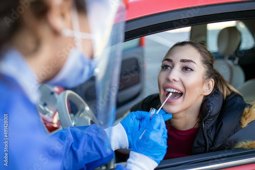 Medical worker performing drive-thru COVID-19 check,taking nasal swab specimen sample from female patient through car window,PCR diagnostic for Coronavirus presence,doctor in PPE holding test kit photo